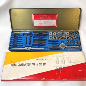 Puede incluir: Un juego de machos de roscar y terrajas de 40 piezas en una caja de metal dorado con interior azul. El juego incluye varios machos de roscar, terrajas y herramientas para roscar. La caja también incluye una caja de cartón amarilla, roja y blanca con el texto "40 PC. COMBINATION TAP & DIE SET".