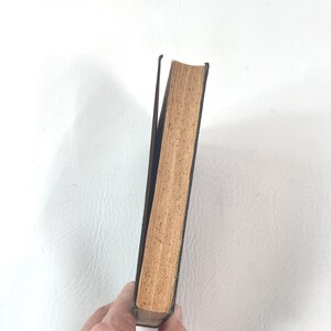 Puede incluir: Un libro antiguo con una cubierta oscura y p&aacute;ginas envejecidas de color marr&oacute;n claro. El lomo es visible, y las p&aacute;ginas muestran signos de desgaste, lo que sugiere una edici&oacute;n antigua o muy usada. El libro se sostiene en &aacute;ngulo.