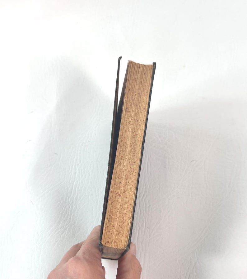 Puede incluir: Un libro antiguo con una cubierta oscura y p&aacute;ginas envejecidas de color marr&oacute;n claro. El lomo es visible, y las p&aacute;ginas muestran signos de desgaste, lo que sugiere una edici&oacute;n antigua o muy usada. El libro se sostiene en &aacute;ngulo.
