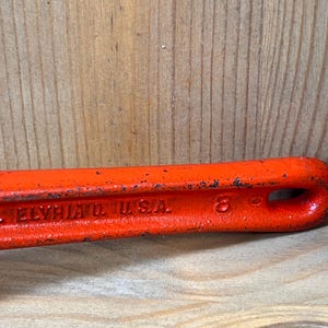 May include: Close-up of a vintage orange wrench with the text "ELYRIA O. USA" and the number "8" embossed on the side. The tool has a loop at the end and shows signs of wear.