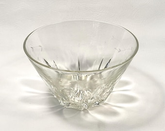 May include: A clear glass bowl with a flared, faceted design. The bowl has etched floral patterns near the rim and a starburst pattern on the base. The bowl is empty and sits on a white surface.