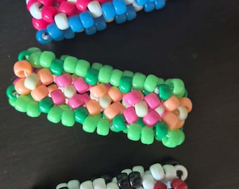 Könnte beinhalten: Drei farbenfrohe Armbänder aus Perlen. Das obere Armband hat blaue, rosa und weiße Perlen. Das mittlere Armband hat grüne, rosa, orange und weiße Perlen. Das untere Armband besteht aus schwarzen, weißen und roten Perlen.