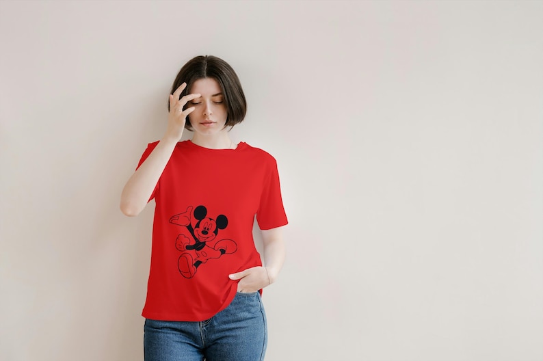 May include: A red t-shirt featuring a black graphic of Mickey Mouse. The shirt is short-sleeved and has a crew neck. The person is wearing blue jeans.