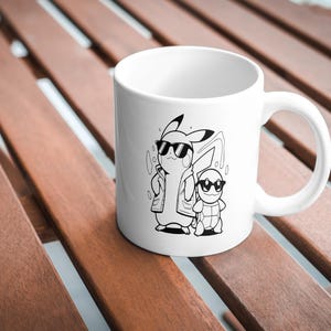 May include: White ceramic mug featuring a black and white illustration of Pikachu and Squirtle wearing sunglasses. The mug has a curved handle and is set against a wooden background. A fun, pop culture themed item.