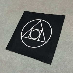 May include: Black square patch featuring a white geometric design. The design includes a circle, a triangle, a square, and a smaller circle. The patch is made of a woven fabric.