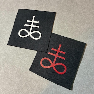 May include: Two square fabric patches in black, each featuring a Leviathan cross symbol. One patch displays the symbol in white, while the other patch features the same symbol in red. Both patches have a visible woven texture and clean edges.