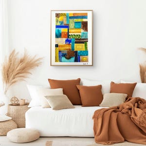 Peut inclure: Impression d'art abstrait dans un cadre doré. L'œuvre présente un motif patchwork avec des carrés et des rectangles dans des tons de bleu, jaune, marron et vert. L'œuvre est exposée au-dessus d'un canapé blanc avec des coussins marron et beige et un plaid assorti.