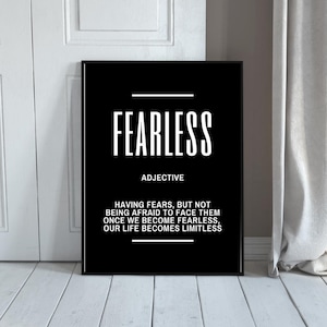 Puede incluir: Un estampado enmarcado en blanco y negro con la palabra "FEARLESS" en letras blancas grandes. Debajo, la definición dice "ADJETIVO" y una cita más larga sobre cómo superar los miedos. El estampado se muestra contra una puerta blanca y una cortina.
