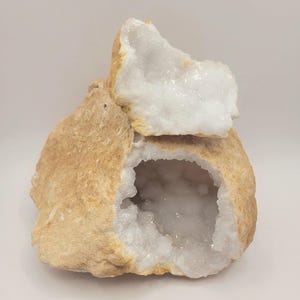 Puede incluir: Geoda con exterior áspero de color marrón claro e interior de cristal blanco brillante. Un trozo de la geoda está roto, revelando la estructura cristalina. El texto "B20" es visible en la esquina inferior derecha.