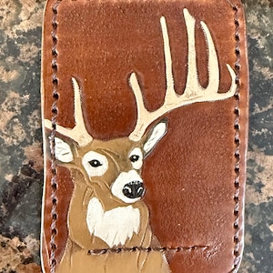 May include: A brown leather wallet featuring a deer design. The deer has white antlers and chest markings. The rectangular wallet has stitched edges and is made of brown leather.