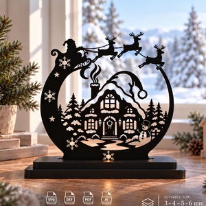 Può includere: Un ornamento decorativo nero tagliato al laser con la sagoma di una casa, un pupazzo di neve e Babbo Natale su una slitta con renne. Il design include fiocchi di neve e stelle all'interno di una cornice circolare su base rettangolare. Testo: SVG DXF PDF AI INSTANT DOWNLOAD SUITABLE FOR 3-4-5-6 mm MATERIAL.