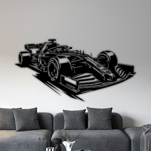 Könnte beinhalten: Schwarze Metall-Wandkunst eines Formel-1-Rennwagens. Das Kunstwerk ist an einer weißen Wand über einem grauen Sofa angebracht. Das Auto wird in einer dynamischen Pose dargestellt, die Geschwindigkeit und Bewegung suggeriert. Das Gesamtthema ist Automobil und Rennsport.