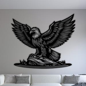 May include: Black metal eagle wall art with outstretched wings, mounted on a white wall. The eagle is perched on a rock, with detailed feathering. The artwork is displayed above a white sofa in a modern living room setting.