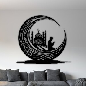 May include: Black metal wall art featuring a mosque silhouette inside a crescent moon, with a praying figure. The artwork is mounted on a white wall above a grey sofa, providing a strong visual contrast.