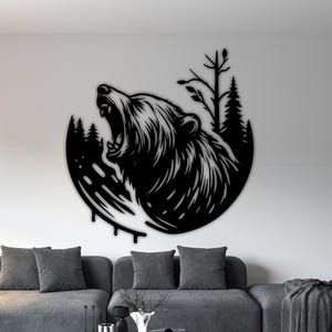 Könnte beinhalten: Schwarze Metall-Wandkunst, die einen brüllenden Bären in einem kreisförmigen Rahmen darstellt. Das Design umfasst stilisierte Bäume und eine Waldsilhouette. Das Kunstwerk ist an einer weißen Wand angebracht.