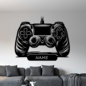 以下が含まれることがあります： 黒い金属製のビデオゲームコントローラーの壁掛けアート。 コントローラーは、詳細なボタンとジョイスティックのデザインが特徴で、下部のパネルには「NAME」という単語が表示されています。 このアートワークは、灰色のソファの上にある白い壁に取り付けられています。