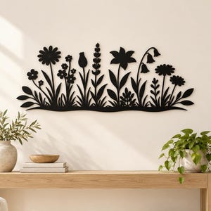 May include: A black metal wall art piece featuring a horizontal silhouette of various wildflowers and stems. The design displays a diverse collection of botanical shapes, including daisies, lavender, and bell-shaped flowers, arranged in a dense row.