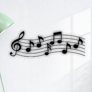 Könnte beinhalten: Schwarze Metall-Wandkunst mit einer Notenlinie, einem Violinschlüssel und Noten. Die Noten variieren in Größe und Form und erzeugen eine dynamische Optik. Das Kunstwerk ist an einer weißen Wand befestigt.