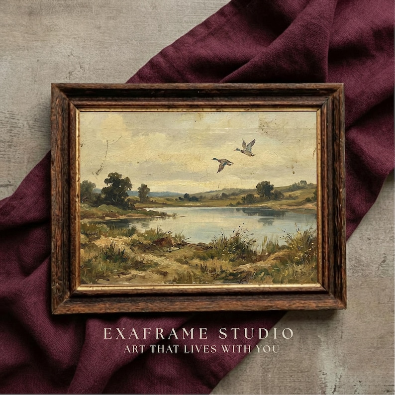 [Mallard Ducks Antique Oil Painting] shown in a detailed close-up within a textured dark wood frame resting on a luxurious Plum Noir fabric backdrop. This mockup highlights the authentic soul of the flying birds and the aged patina of the vintage wetland landscape. The lighting emphasizes the fine art canvas texture and painterly details, making it a perfect gift for nature lovers and vintage collectors — see every detail and download instantly.