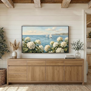 A cozy coastal farmhouse setting where the TV art sits above a long rustic wooden dresser. The warm wood tones of the furniture beautifully complement the cool blue ocean hues and white floral textures of the painting. This scene illustrates how well the grandmillennial aesthetic blends with organic materials and traditional home styling. Bring a touch of the Nantucket shore to your living space—buy this digital art and start decorating.
