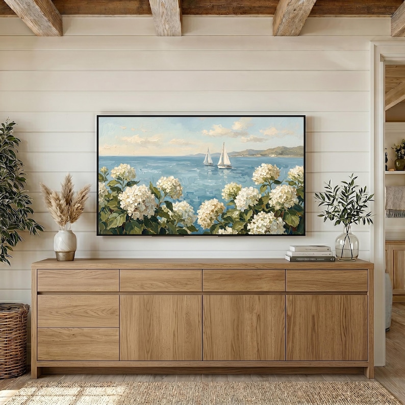 A cozy coastal farmhouse setting where the TV art sits above a long rustic wooden dresser. The warm wood tones of the furniture beautifully complement the cool blue ocean hues and white floral textures of the painting. This scene illustrates how well the grandmillennial aesthetic blends with organic materials and traditional home styling. Bring a touch of the Nantucket shore to your living space—buy this digital art and start decorating.
