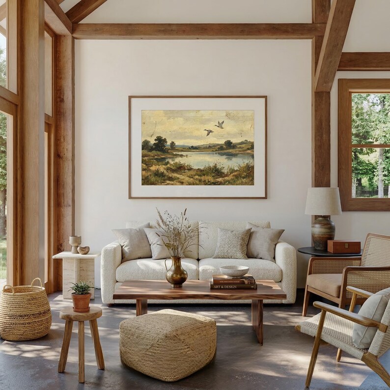 [Country Home Decor] vintage wildlife painting shown in a large-scale format in a sun-drenched, open-concept living room with high ceilings and exposed wooden beams. The lake landscape art is the focal point above a white textured sofa, surrounded by rattan furniture and natural light. This grand lifestyle scene demonstrates the versatility of our printable digital art for oversized statement pieces — bring calm artistry to your walls instantly.
