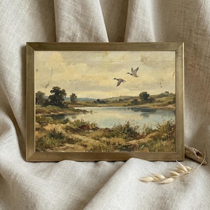 [Vintage Duck Art] presented in a thin minimalist gold frame resting on a soft, draped linen backdrop. The close-up view emphasizes the muted, earthy tones of the mallard ducks and the atmospheric depth of the wetland landscape. This elegant presentation highlights the "Fine Art" quality and museum-worthy finish of the digital download, making it a perfect gift for art collectors — download beautiful art for your home instantly.