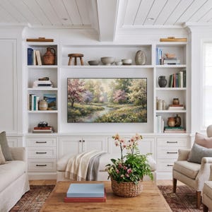 A luxurious custom living room featuring built-in white bookshelves framing a tranquil spring meadow TV art display. The cozy central seating area includes a wooden coffee table styled with books and a fresh floral basket, creating a sophisticated gallery wall ambiance. Transform your entertainment center into a fine art showcase—click to download your digital file now.