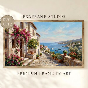 May include: A framed landscape painting depicts a coastal scene with a stone pathway, buildings, and the sea. Pink flowers cascade over a building's entrance. The artwork includes the text "EXAFRAME STUDIO" and "PREMIUM FRAME TV ART".