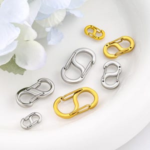 May include: A collection of S-shaped carabiner clips in various sizes, featuring both gold-tone and silver-tone metal finishes. Each clip has a spring-loaded gate mechanism on both ends, allowing for secure attachment of items to keychains or bags.