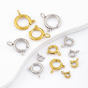 May include: A collection of round spring ring clasps in various sizes, featuring both gold-toned and silver-toned metal finishes. Each clasp includes a small circular loop for attachment and a spring-loaded mechanism for opening and closing.