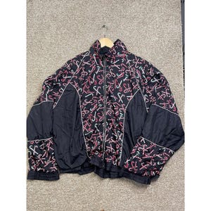 Puede incluir: Chaqueta negra con cremallera y estampado de bastones de caramelo en rosa, blanco y verde. La chaqueta tiene cuello alto, ribete blanco y paneles negros en las mangas y laterales. Una prenda exterior festiva.