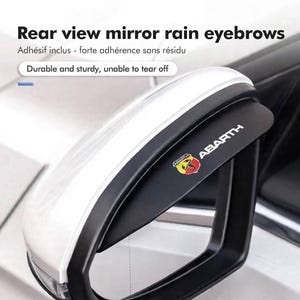 Könnte beinhalten: Ein schwarzer Regenschutz für Autoseitenspiegel mit dem Abarth-Logo und Schriftzug. Das Zubehör ist am oberen Rand des Seitenspiegelgehäuses eines weißen Fahrzeugs angebracht. Der Text Rear view mirror rain eyebrows und Durable and sturdy ist sichtbar.