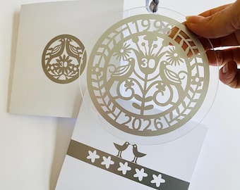 May include: A circular clear acrylic ornament featuring a laser-cut design of two birds, a central flower with the number 30, and the years 1996 and 2026. The ornament hangs from a grey ribbon and is displayed alongside white stationery with matching graphics.