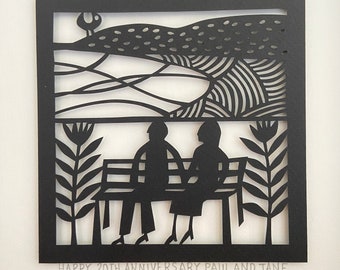 May include: Black and white paper cut-out art depicting a couple sitting on a bench in a park. The background features a stylized landscape with hills and trees. The text "HAPPY 20TH ANNIVERSARY PAUL AND JANE" is at the bottom of the image.