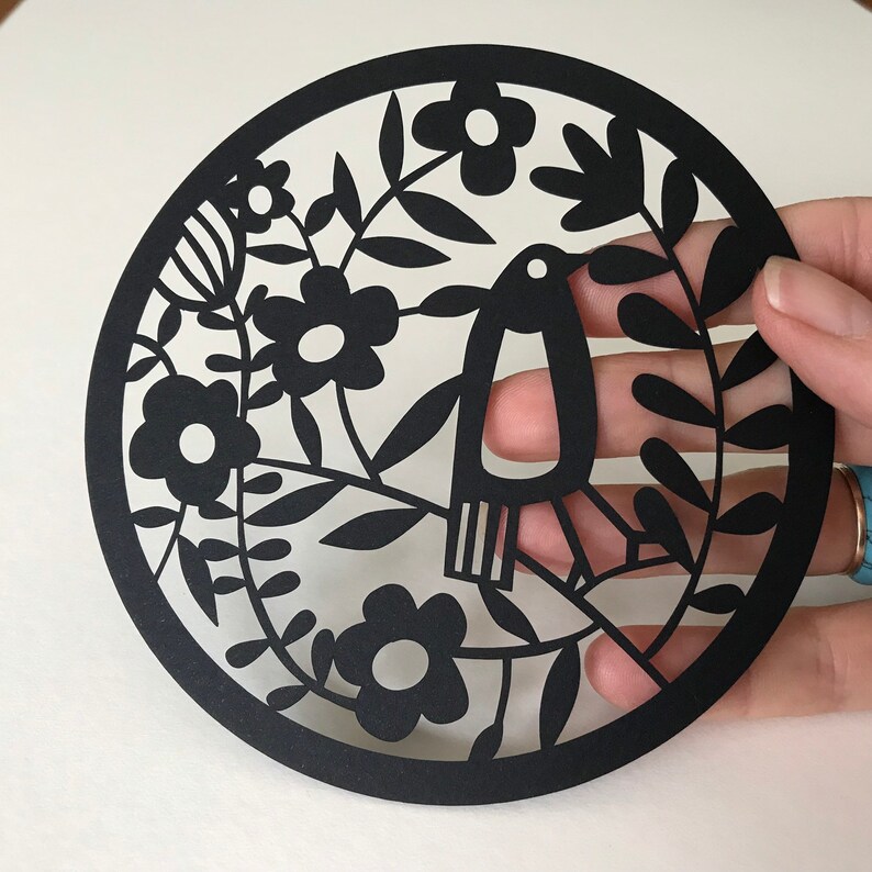 May include: Black paper cut-out design of a bird with flowers and leaves. The design is intricate and detailed, with a delicate silhouette.