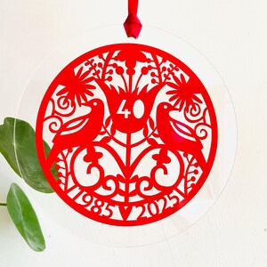 May include: Red paper cut-out ornament with a floral design, two birds, and the numbers 40, 1985, and 2025.