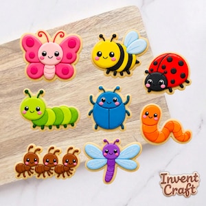 May include: A collection of eight colorful insect-shaped cookies featuring a pink butterfly, yellow bee, red ladybug, green caterpillar, blue beetle, orange worm, three brown ants, and a purple dragonfly, with the text Invent Craft in the corner.