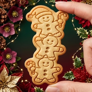 May include: A light brown cookie shaped like a vertical stack of three gingerbread figures. The top figure wears a Santa hat and holds a candy cane, the middle figure has arms raised, and the bottom figure holds a candy cane. The cookie has embossed details.