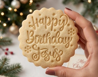 May include: A round, scalloped-edge sugar cookie featuring the embossed text "Happy Birthday Jesus" in a cursive script. The cookie is decorated with small, stamped snowflake and star patterns surrounding the central lettering.