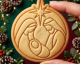 May include: A round, light brown cookie featuring an embossed nativity scene. The design depicts two figures leaning over a central infant, all positioned beneath a prominent star. The cookie has a smooth, baked texture with clean, defined lines.