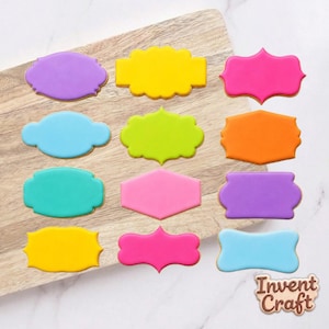 May include: A collection of colorful, frosted cookies in various shapes, including ovals, rectangles, and decorative frames. The cookies are arranged on a wooden cutting board, with a white marble surface in the background. The cookies are in shades of purple, yellow, pink, blue, green, and orange.