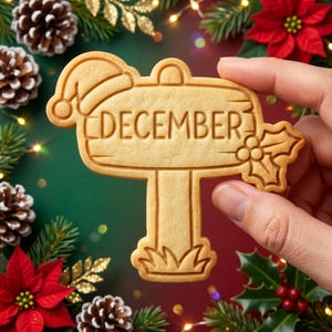 以下が含まれることがあります： 中央に「DECEMBER」という文字が刻印された、看板型の薄茶色のクッキー。左上隅にはサンタクロースの帽子、右側にはヒイラギの葉のモチーフがあしらわれており、土台部分には草の模様が施されています。