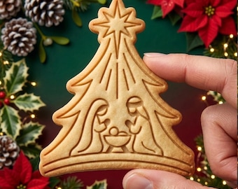 May include: A light brown, tree-shaped cookie featuring an embossed nativity scene. The design depicts two figures kneeling beside a manger, topped with a large star. The cookie has a smooth, baked texture with clearly defined, recessed lines.