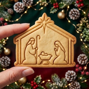 May include: A light brown, house-shaped cookie featuring an embossed nativity scene. The design depicts two figures kneeling on either side of a central manger with a baby, all beneath a large star at the peak of the roof-shaped cookie structure.