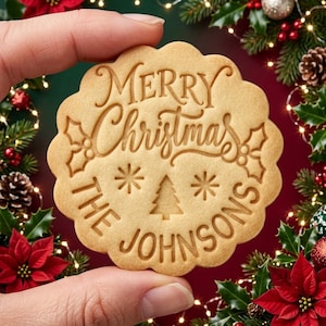Könnte beinhalten: Ein runder Keks mit gewelltem Rand und einer Prägung, die Merry Christmas, The Johnsons zeigt, ergänzt durch Stechpalmenblätter, Sternchen und ein kleines Tannenbaumsymbol auf der hellbraunen, gebackenen Oberfläche.