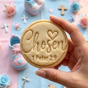 May include: A round, beige sugar biscuit featuring the embossed text "Chosen" with a heart icon above it and the scripture reference "1 Peter 2:9" below. The biscuit has a smooth, baked surface and a raised border around the circular edge.
