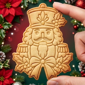 May include: A light brown, flat, nutcracker-shaped cookie with embossed details including a tall hat, a mustache, a beard, and a bow. The cookie features decorative holly leaves and berries on the sides and top, with a smooth, baked texture.