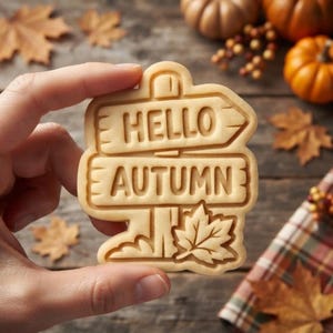 May include: A light beige cookie cutter shaped like a double-sided wooden signpost with the embossed text HELLO AUTUMN and a maple leaf detail at the bottom. The design features two horizontal rectangular signs stacked vertically on a central post.