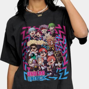 May include: Black t-shirt featuring a colorful graphic of anime characters. The design includes the text "Undead Unluck" in blue and green. The background has a pink and blue zigzag pattern.